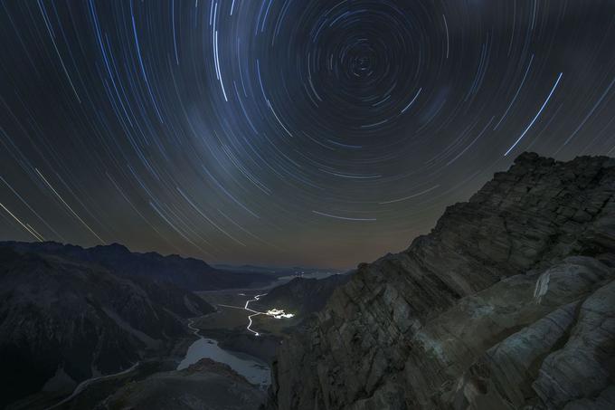 Fotografija je nastala v bližini najstarejše planinske koče v novozelandskem nacionalnem parku Mount Cook. Fotografu Leeju Cooku je uspelo z dalj časa odprto zaslonko fotoaparata ujeti ples svetlobnih sledi zvezd nad bližnjo vasico. Foto: Lee Cook. | Foto: 