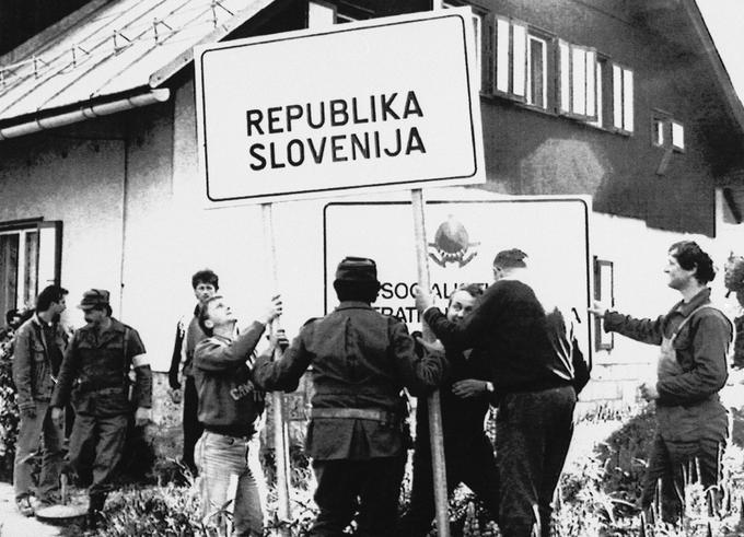 Slovenski teritorialci in civilisti odstranjujejo tablo z napisom Socialistična federativna republika Jugoslavija in postavljajo tablo z napisom Republika Slovenija. Fotografija je bila posneta po slovenskem zavzetju mejnega prehoda Jezersko 29. junija 1991. | Foto: Guliverimage/Vladimir Fedorenko