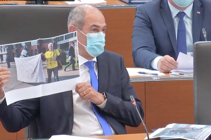 Janša | Janez Janša v državnem zboru kaže fotografijo, na kateri je protestnik Igor Bricelj pred stavbo DZ s transparentom Smrt janšizmu, svoboda narodu. | Foto zajem zaslona