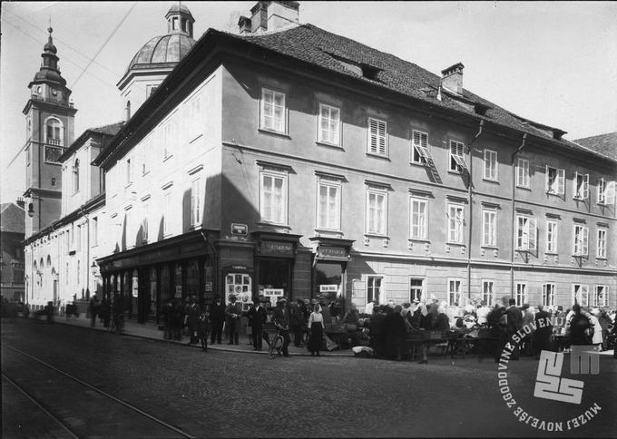 Del tržnice na Vodnikovem trgu med obema vojnama, levo je izložba Jugoslovanske knjigarne, na vogalu oglasna vitrina ateljejskega fotografa Frana Grabjeca. V pritličju vogalne hiše, kjer je nekoč bila knjigarna, je danes trgovina s turističnim kičem in spominki. | Foto: neznan, arhiv MNZS