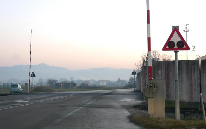 Železniški prehod podnevi. Na levi strani je vidna bela telefonska omarica, v kateri morajo ročno aktivirati zapornice pred prihodom tovornega vlaka. | Foto: Gregor Pavšič