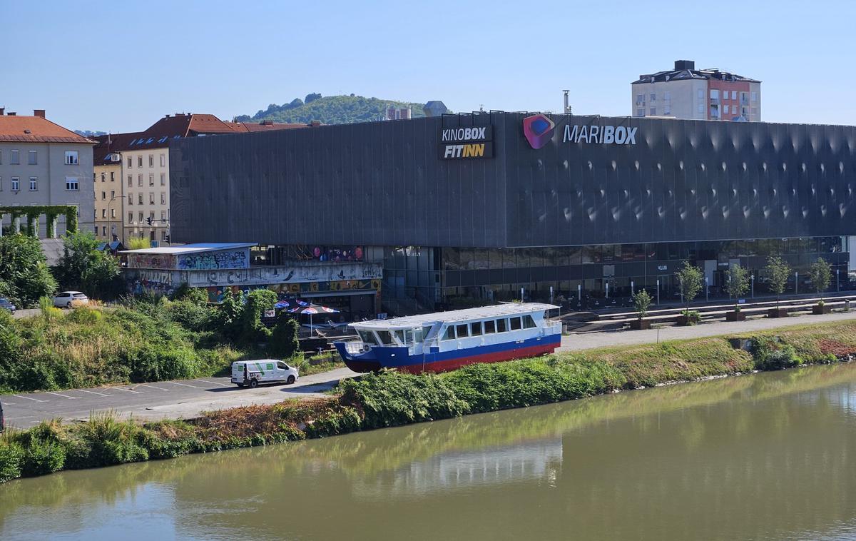 Ladijca v Mariboru | Pred kratkim so okoli 22 metrov dolgo in skoraj 40 ton težko ladjo na nabrežju, poleg katerega leži občinsko parkirišče, prebarvali na belo, modro in rdečo.  | Foto STA